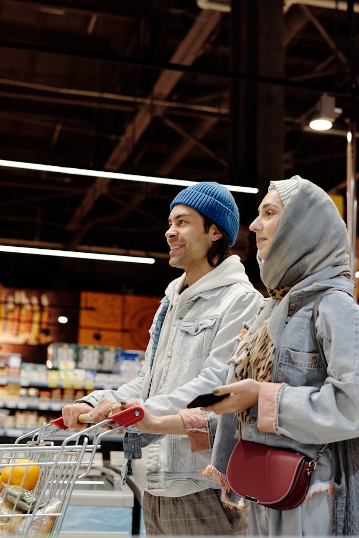 A smiling couple shopping in a supermarket, pushing a cart and enjoying their time together.